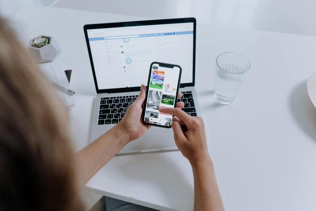 Person using both a smartphone and laptop, multitasking at a modern desk with office plants.